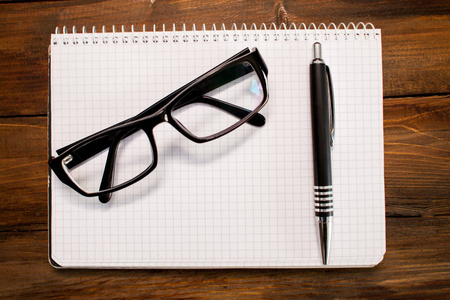 与白页框中的记事本，在黑色的玻璃眼镜框架和钢笔上木制的背景。顶视图