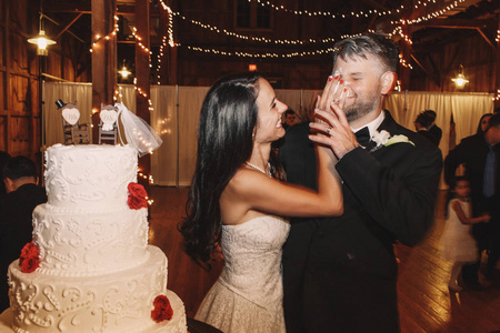 微笑黑发新娘在新郎的脸上放一个婚礼蛋糕