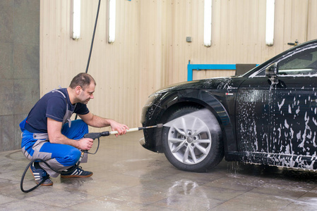 一个男人用泡沫洗一辆黑色的汽车。