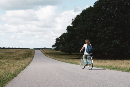 微笑的年轻漂亮的女人骑自行车在乡村的小路上