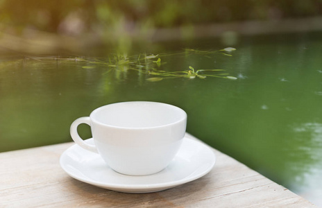 木桌上有绿色池塘背景的咖啡杯