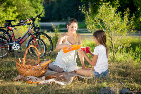 幸福的母亲和女儿在野餐会上喝橙汁