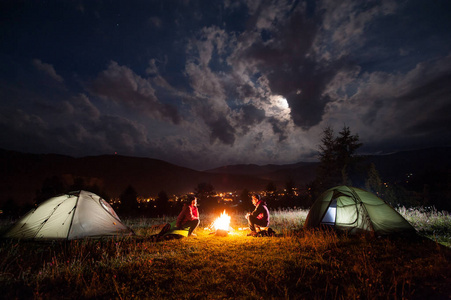 男人和女人坐在靠近两个帐篷在夜里