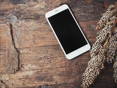 智能手机的顶部视图与空白屏幕和美丽的干花在木桌上
