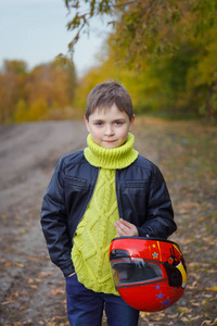 一个男孩在一件皮夹克与头盔在一个秋天的树林背景他手中的画像