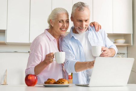 幸福成熟爱夫妇的家庭饮用茶使用的便携式计算机