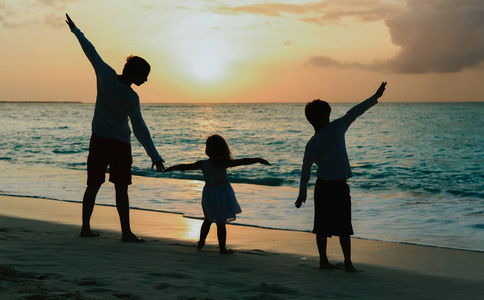 父亲与儿子和女儿剪影戏剧在日落海滩