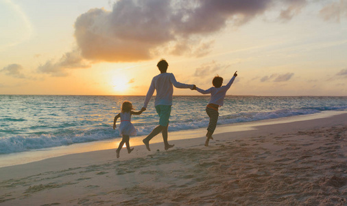在日落时在沙滩上玩的两个孩子的父亲