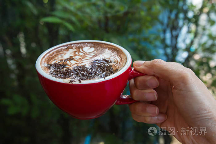 一个手拿着红色的一杯热咖啡