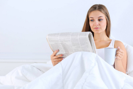 年轻漂亮的女人在床上看报，享受一杯茶