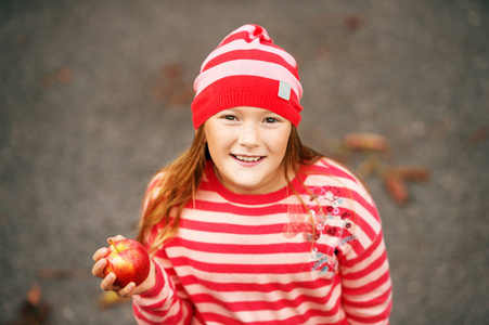 秋天的可爱的小女孩抱着红红的苹果，穿着条纹帽子和毛衣的肖像