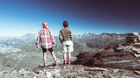 几名徒步旅行者在山顶上，看着 expasnive 视图和山的山峰。在阿尔卑斯山的夏天冒险。从上面的广角视图色调图像，后视