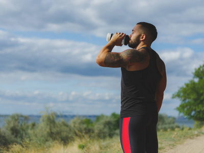 一个强健美运动员肌肉发达的身体与自然模糊背景上运动后的纹身喝水