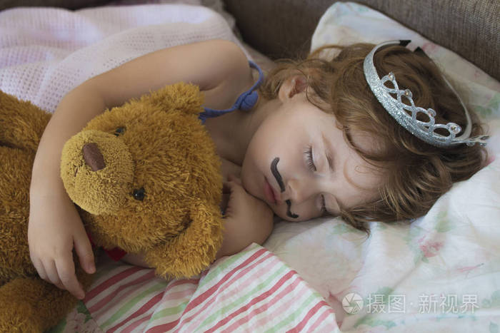 特写肖像小女孩睡在床上.皇冠公主躺在床上抱着泰迪熊