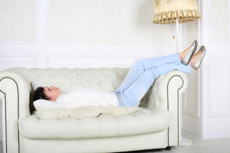 穿着白色毛衣和牛仔裤的快乐女人躺在沙发上