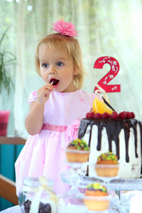 女孩生日。两年的白叟小姑娘正在一个生日蛋糕。小女孩庆祝第二个生日