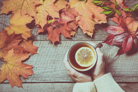 喝杯茶的手里的柠檬，色彩鲜艳的秋叶在木板上。秋季静物，复古风格。顶视图。遮罩效果