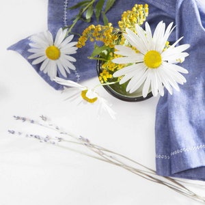 在白色搪瓷杯子和白色的木桌上的蓝色餐巾 th 雏菊