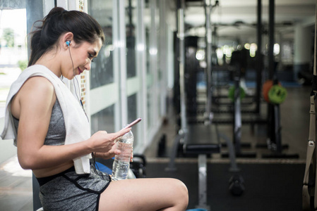 年轻的运动型女人在健身房的智能手机上听音乐