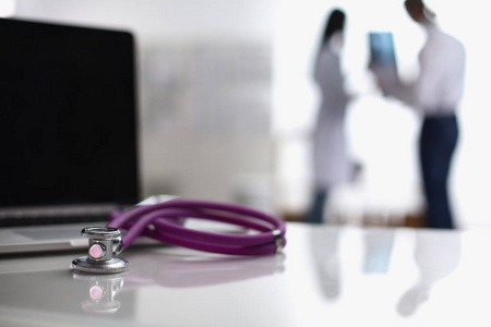 笔记本电脑和医用听诊器在桌上，站在后台的医生