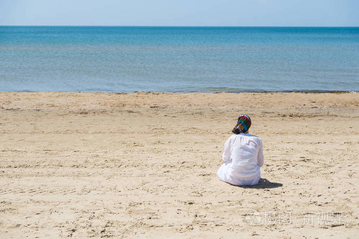 孤独的黑发女人, 戴着围巾坐在海滩上, 看着大海.后视图