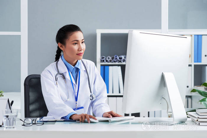 在办公室电脑工作的年轻女医生画像照片-正版商用图片