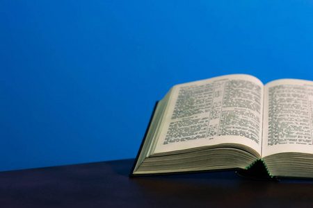 在黑色的玻璃桌上打开圣经。美丽的蓝色背景。宗教概念