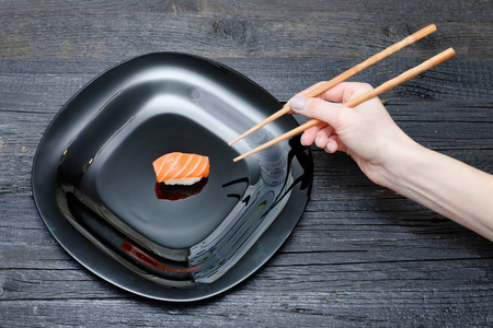 女性手用筷子和寿司。黑木背景