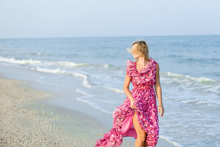 美丽的年轻苗条的女孩运行在沙滩上海边。穿着一条长玫瑰裙。波.在海的背景下。度假.阳光.文本位置