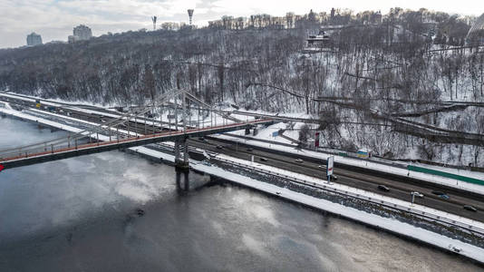 在冬季和第聂伯河河上的行人公园大桥的空中俯视图, 位于乌克兰基辅地平线上的雪基辅城市景观