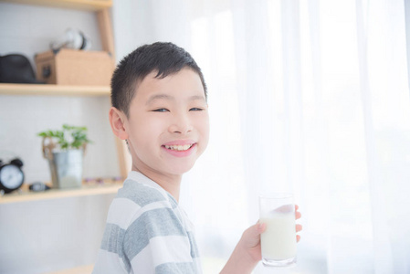 年轻的亚洲男孩拿着一杯牛奶和微笑在照相机