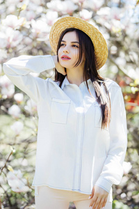美丽的年轻女子的画像在夏天帽子和太阳镜与玉兰花树