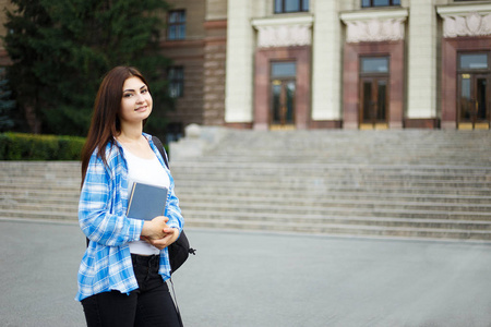 微笑的学生女孩与书和背包站立在大学校圆