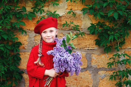 美丽的小女孩与一束丁香花。穿红毛衣的时髦女孩