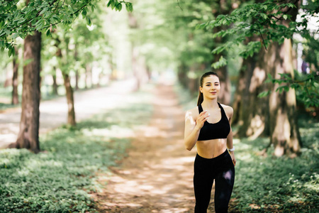 年轻的微笑运动的女人在公园里奔跑。健身女孩公园慢跑