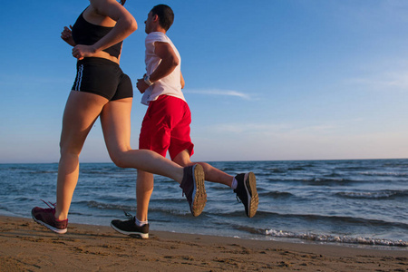 日落时分热带海滩慢跑青年夫妇的低断面观
