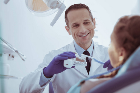 快活的男性牙医示范牙齿清洁模型