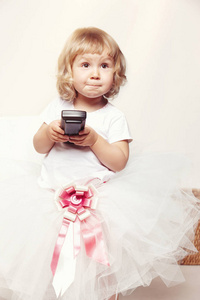 一个可爱的小女孩的肖像在白色的礼服举行电视遥控器在白色背景