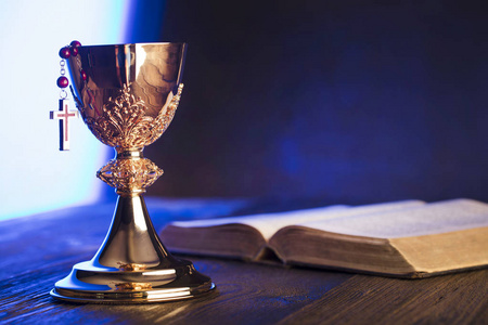 罗马天主教教堂的主题。圣洁圣经, 念珠和金黄圣杯在褐色木桌