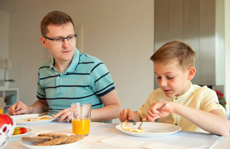 愉快的年轻父亲与他的可爱的小儿子在早餐讲话