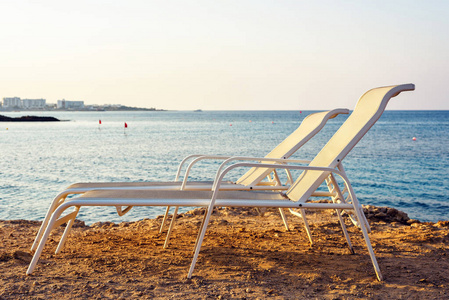 日落视图从一侧到两个平行 sunchairs 放置在水附近。蓝色海与镇在背景。负拷贝空间, 文本位置。Protaras, 塞浦路