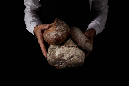 在黑色背景下夹持不同类型面包的围裙上的男面包师的部分观点
