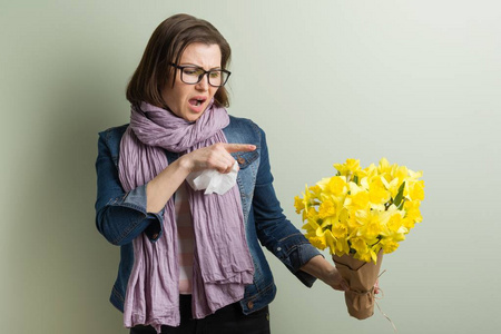 春季对花粉过敏。带着一束黄色花朵的女人要打喷嚏。背景绿色哑光墙