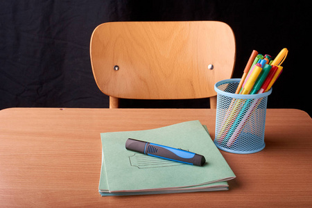 黑色背景下学校书桌上蓝色金属篮中的彩色钢笔