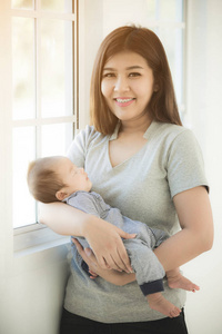 年轻的亚洲母亲温柔地抱着睡在婴儿的肩膀上的孩子 iat 回家