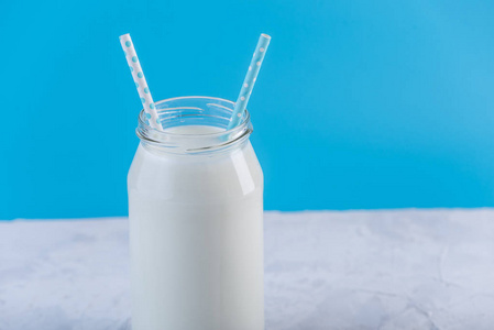 在蓝色背景下用两根吸管的鲜牛奶玻璃瓶。多彩简约。健康乳制品与钙的概念