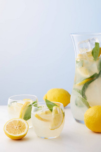 壶和两杯柠檬水与薄荷叶, 冰块和柠檬片在蓝色背景