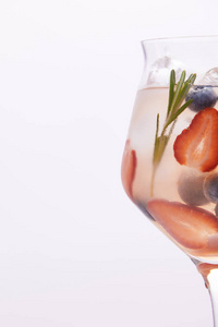 在白色背景下分离的迷迭香蓝莓和草莓的柠檬水玻璃的部分视图