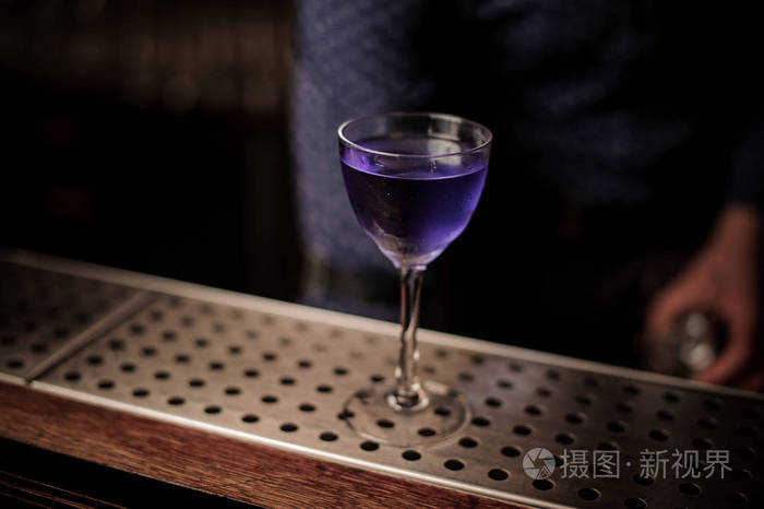 优雅的玻璃充满紫罗兰色的甜美和浓郁的夏日鸡尾酒在酒吧柜台上