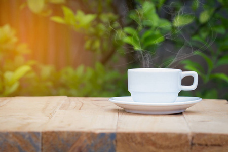白色咖啡杯在木桌上, 绿色植物背景模糊。Copyspace